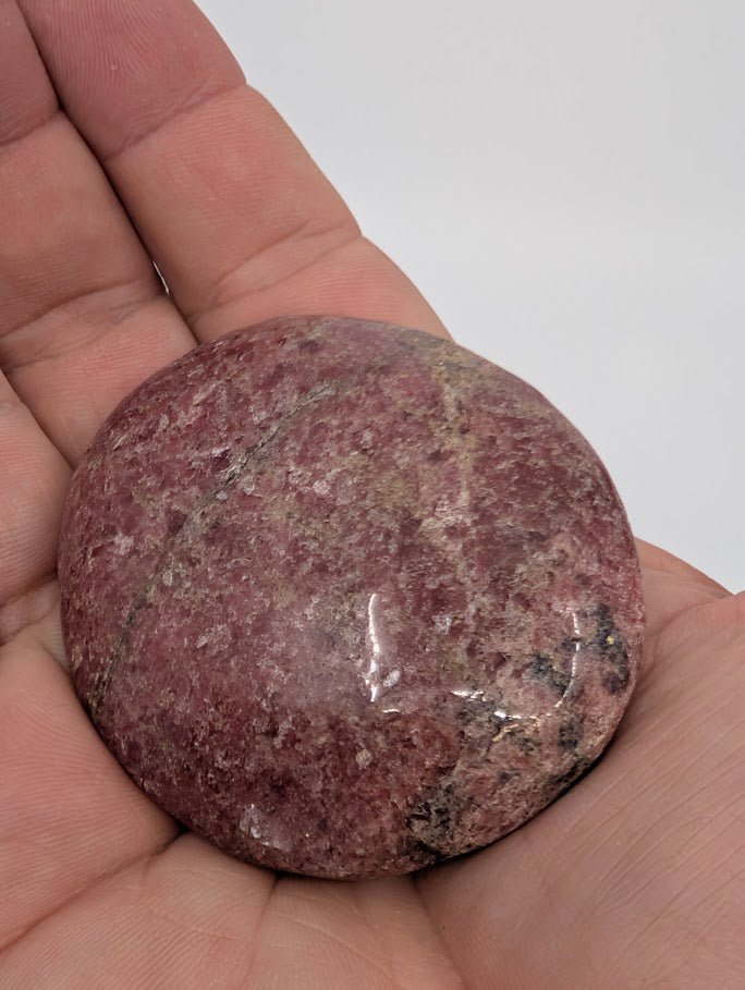 Rhodonite palm stone in hand to show size, polished finish, and natural color zoning