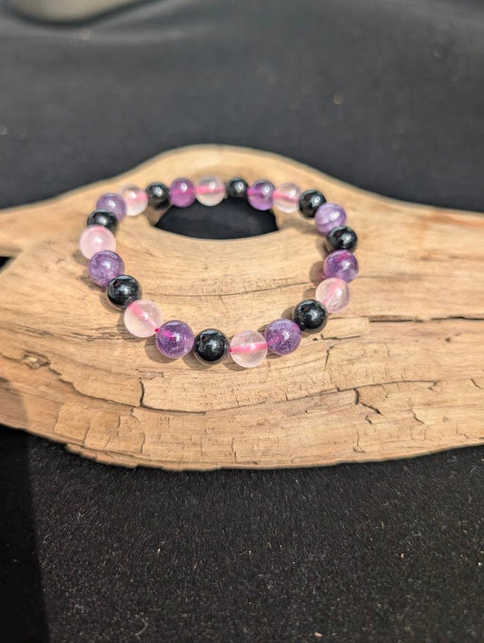 8mm Rose Quartz, Amethyst, and Obsidian beaded bracelet resting on a driftwood display.