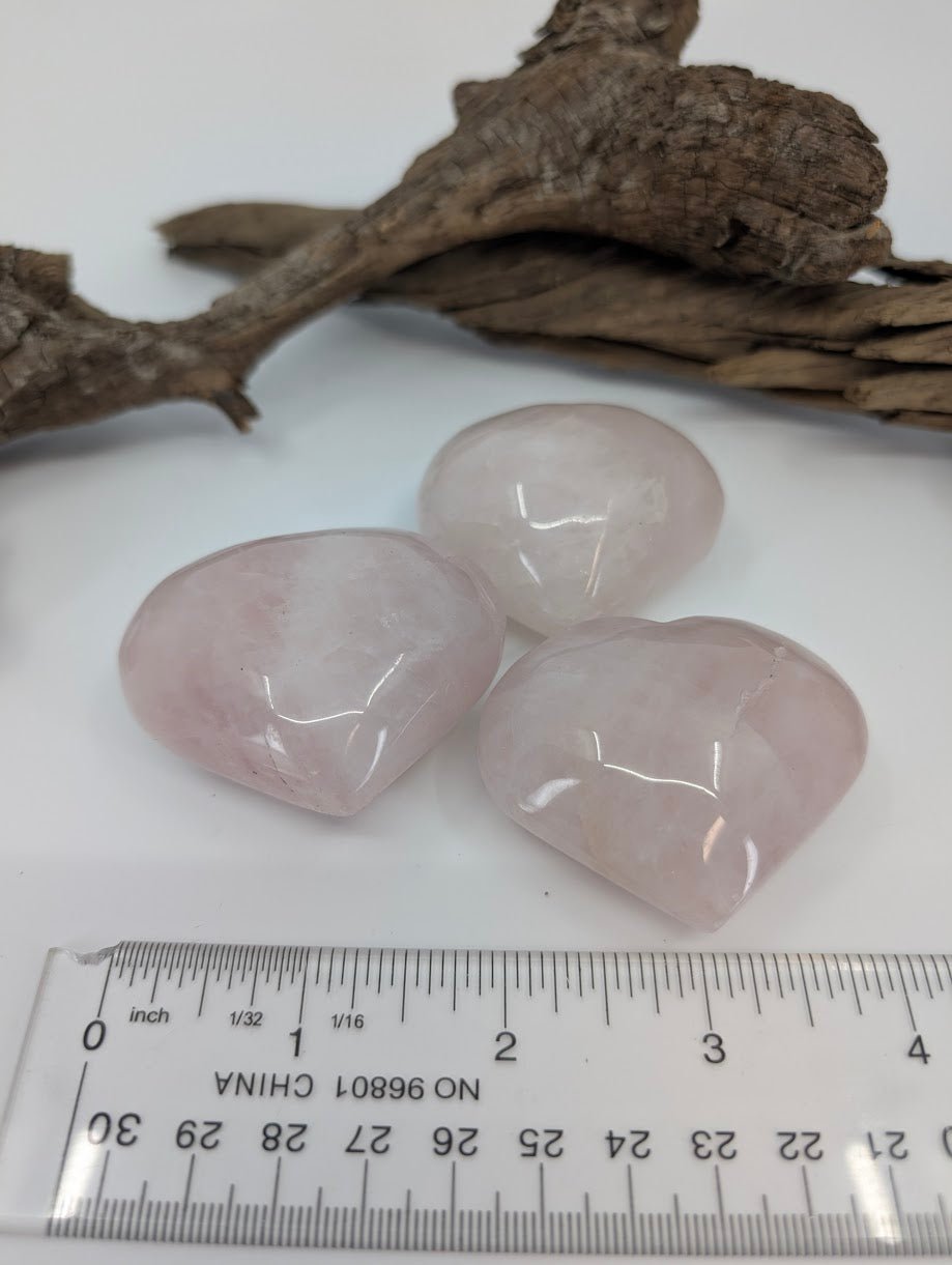 Angle view of three Rose Quartz hearts showing thickness and soft pink color.
