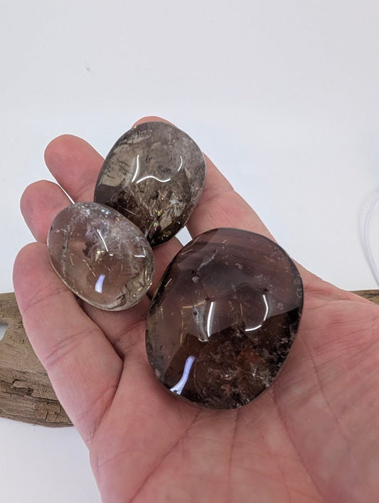 Small, medium, and large Lwena Smokey Citrine palm stones held in hand for scale.