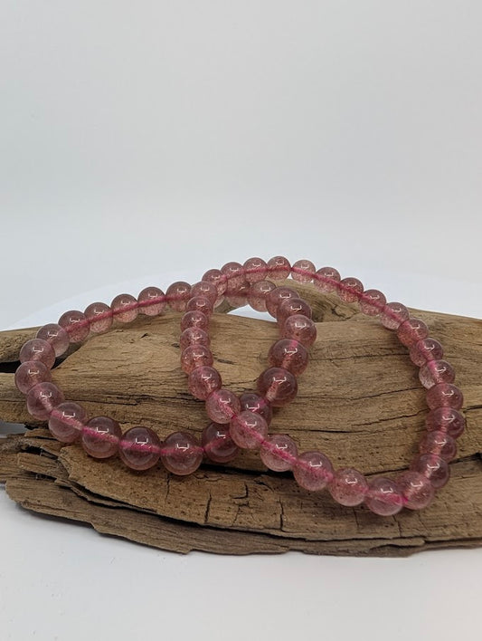 Strawberry Quartz bracelets in 6mm and 8mm displayed on driftwood with berry-pink sparkle