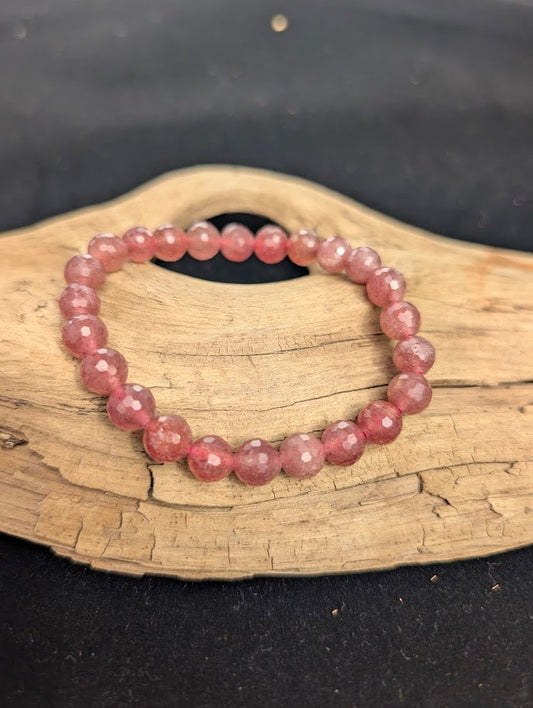 8mm faceted Strawberry Quartz beaded stretch bracelet resting on a driftwood display, showing soft pink colouration.