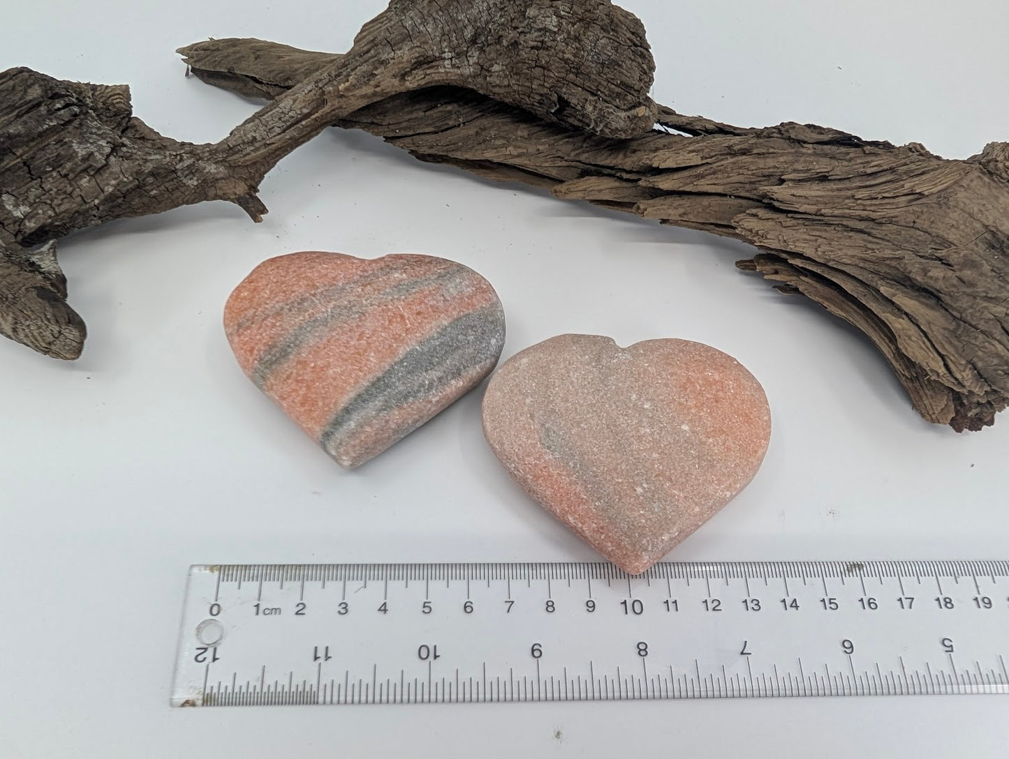 Two polished Peach Sunstone hearts displayed on driftwood.