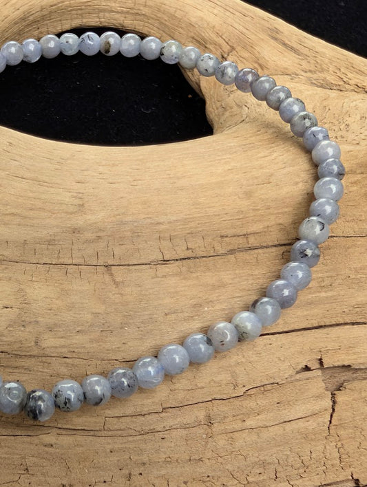 Macro close-up of 3mm polished Tanzanite beads highlighting the high-gloss finish, soft violet-blue hues, and natural dark inclusions.