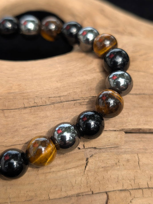 Macro view of polished 8mm Tiger Eye, Hematite, and Obsidian spherical beads on driftwood, highlighting the natural chatoyancy and metallic luster.