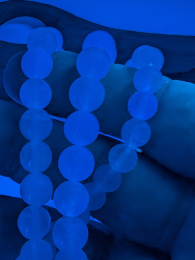 Handheld Velvet Fluorite bracelet glowing blue under UV light showing even transparency