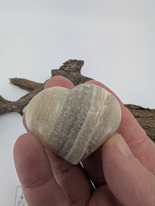 Hand holding a 75g Zebra Calcite heart showing waxy luster and layers.