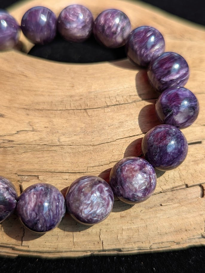 Macro view of a 12mm AAA Charoite beaded bracelet highlighting smooth spherical lapidary polish and pearlescent chatoyant flashes.