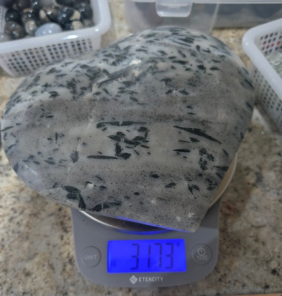 Polished quartz heart on a digital scale displaying a weight of 3173 grams for collector transparency.