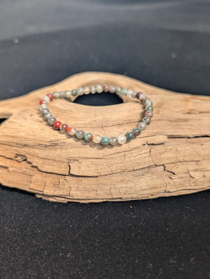 Delicate 4mm African Bloodstone beaded bracelet resting on natural driftwood, displaying earthy green, translucent grey, and red colours.