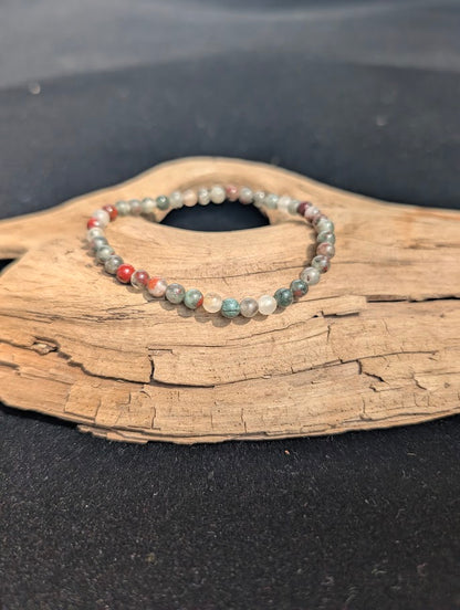 Delicate 4mm African Bloodstone beaded bracelet resting on natural driftwood, displaying earthy green, translucent grey, and red colours.