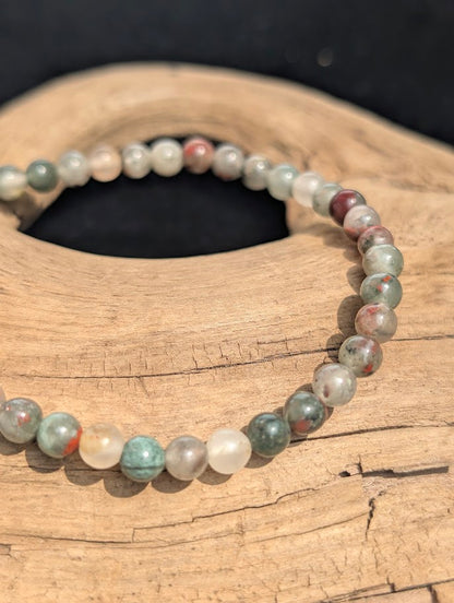 Macro view of polished 4mm African Bloodstone spherical beads on driftwood, highlighting the natural chalcedony and jasper matrix.