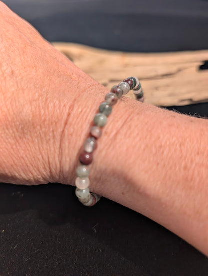 Natural sunlight on a delicate 4mm earthy green and red African Bloodstone stretch bracelet worn on a wrist.