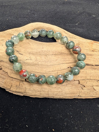 mm faceted African Bloodstone beaded stretch bracelet resting on a driftwood display, showing mottled green and grey stones with red inclusions.