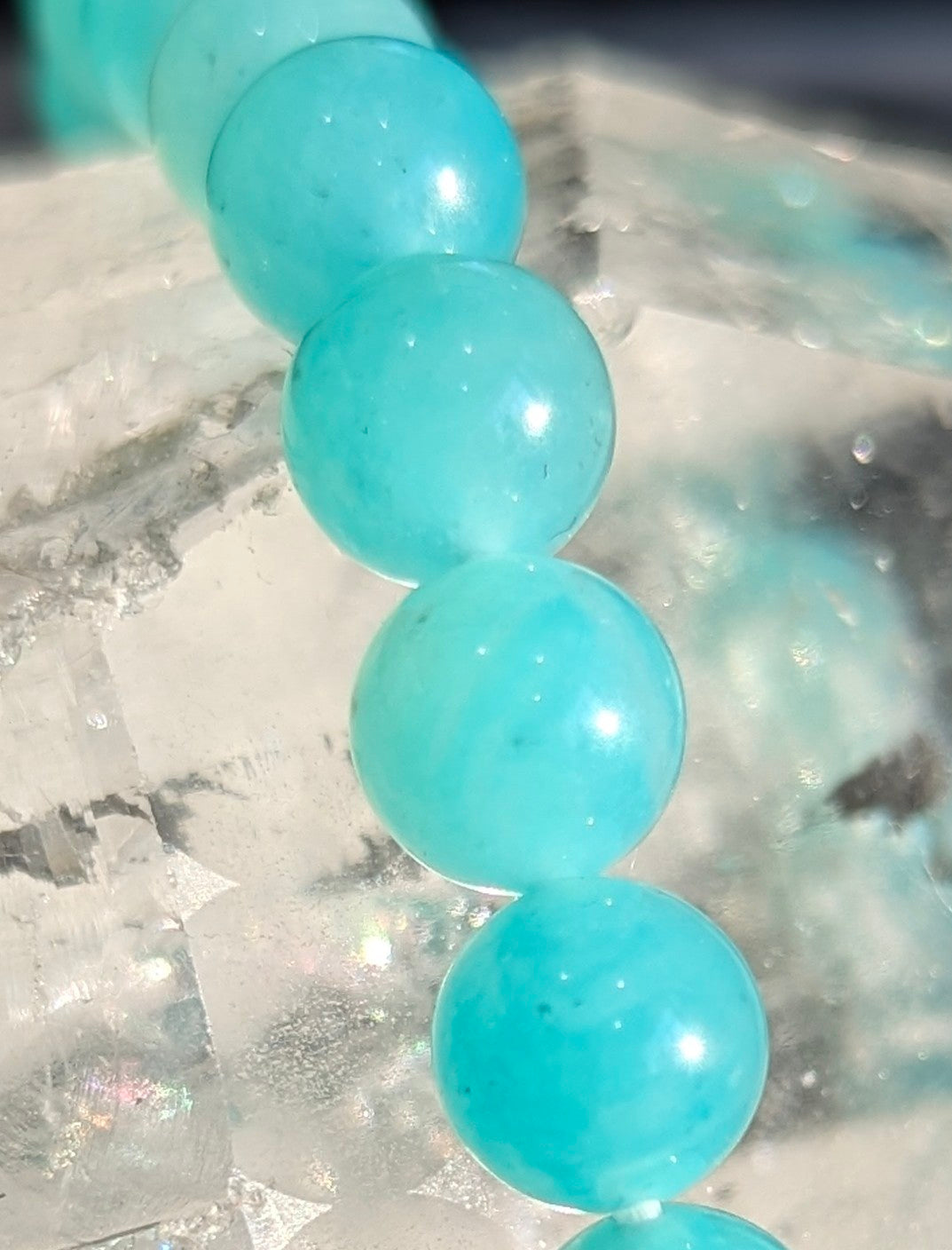 Detailed portrait view of an all-natural 8mm Amazonite stretch bracelet resting on a display surface, showcasing the intense, unaltered blue-green saturation and fine structural mineral banding.