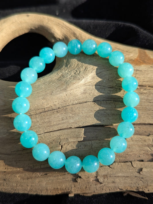 An 8mm Amazonite round bead stretch bracelet positioned on a flat presentation surface, demonstrating bead uniformity, rich turquoise-blue colouration, and natural white perthitic inclusion