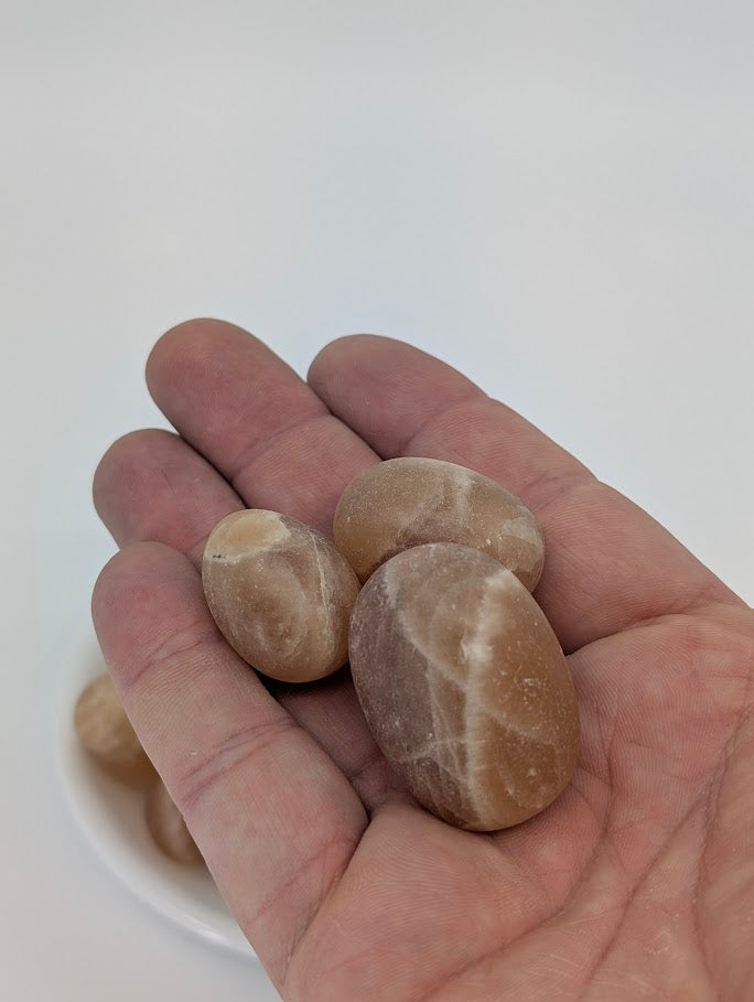 Amber Calcite stones shown in hand for size reference