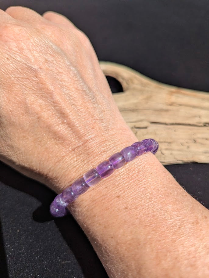 Polished 7mm Amethyst barrel bead stretch bracelet worn on a wrist for size scale.