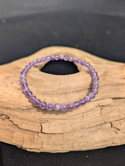 Delicate 4mm Amethyst beaded bracelet resting on natural driftwood, displaying translucent soft lavender and medium purple colors.