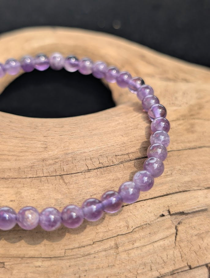 Macro view of polished 4mm Amethyst spherical beads on driftwood, highlighting natural internal quartz veils and color zoning.