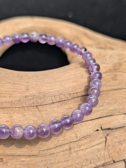 Macro view of polished 4mm Amethyst spherical beads on driftwood, highlighting natural internal quartz veils and color zoning.
