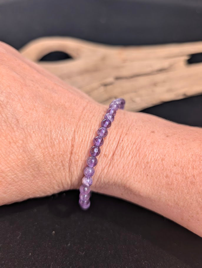 Natural sunlight on a delicate 4mm purple Amethyst stretch bracelet worn on a wrist.