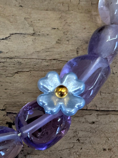Macro close-up of a light blue iridescent flower charm and polished purple Amethyst beads on a handcrafted wire bracelet