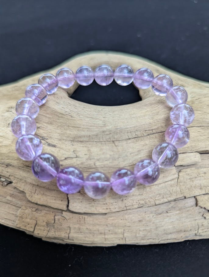 10mm High Quality Brazilian Amethyst beaded stretch bracelet displayed on driftwood, showing uniform polished lavender stones.