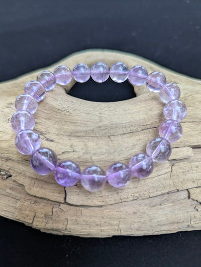 10mm High Quality Brazilian Amethyst beaded stretch bracelet displayed on driftwood, showing uniform polished lavender stones.