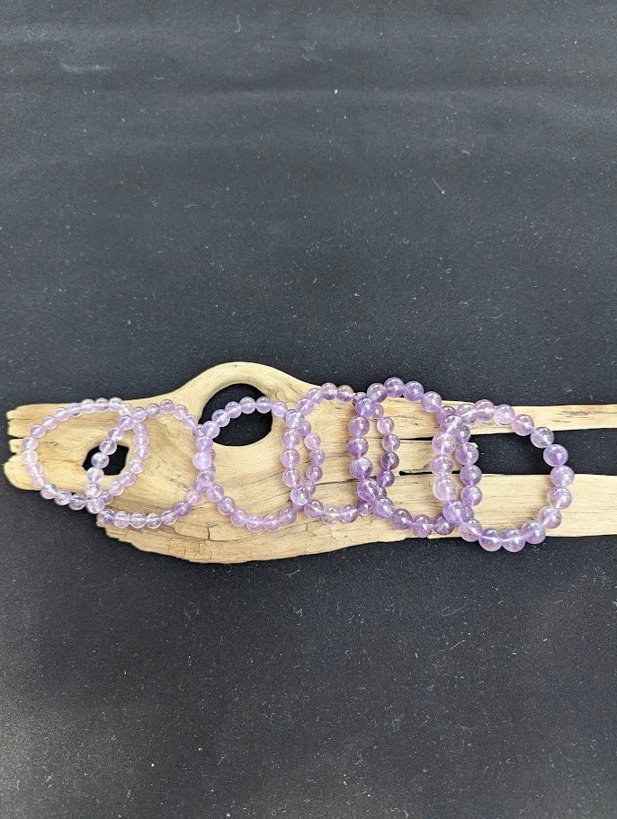 Suite of six High Quality Brazilian Amethyst beaded bracelets displayed side-by-side on driftwood showing sizes 7mm through 12mm.