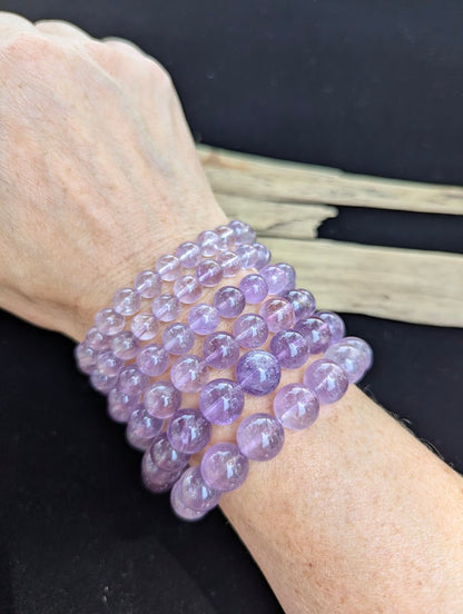 Stack of six High Quality Brazilian Amethyst beaded bracelets worn together on a wrist demonstrating size progression from 7mm to 12mm.