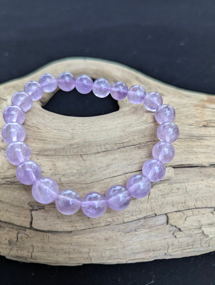 9mm High Quality Brazilian Amethyst beaded stretch bracelet resting on driftwood, showcasing soft violet tones.