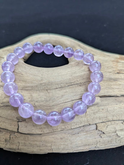 9mm High Quality Brazilian Amethyst beaded stretch bracelet resting on driftwood, showcasing soft violet tones.