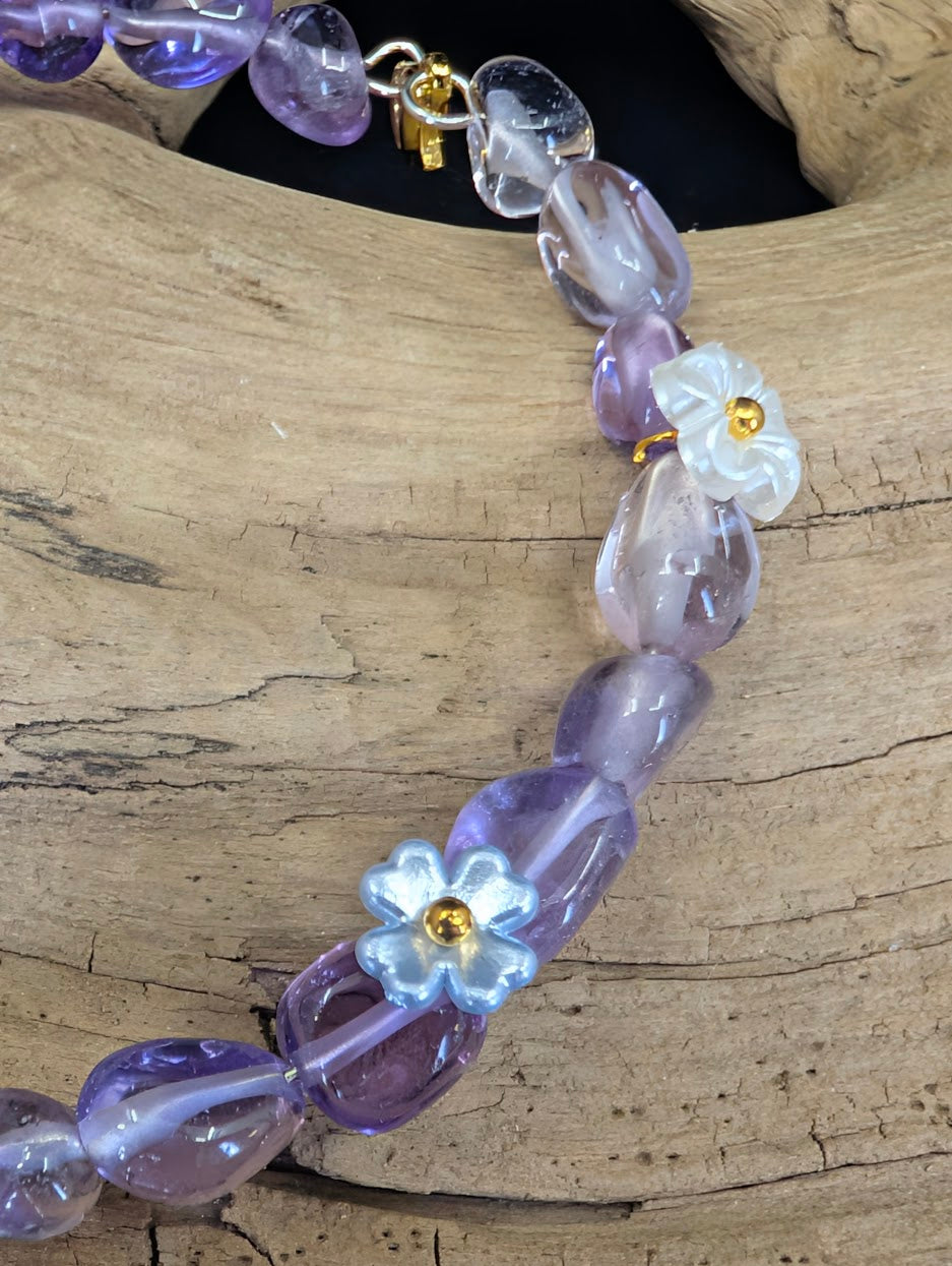 Close-up detail of white and blue floral charms interspersed with natural Amethyst freeform beads on a gold-toned wire.
