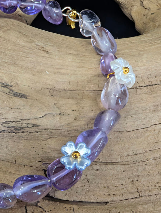 Close-up detail of white and blue floral charms interspersed with natural Amethyst freeform beads on a gold-toned wire.