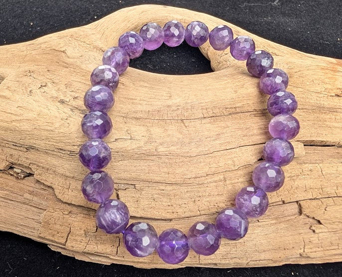 8mm faceted Amethyst beaded stretch bracelet resting on a driftwood display, showing deep violet and lavender tones.