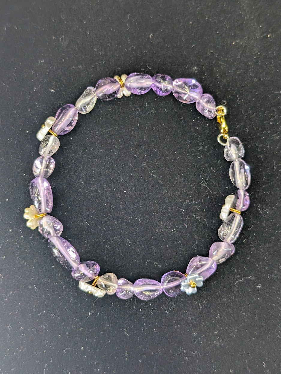 Top-down view of the Amethyst and flower charm bracelet laid in a circle against a high-contrast black background.