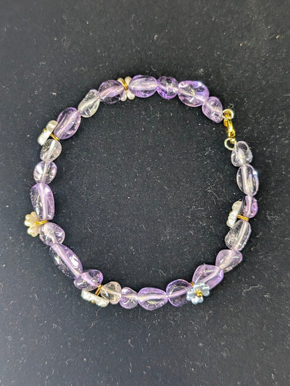 Top-down view of the Amethyst and flower charm bracelet laid in a circle against a high-contrast black background.