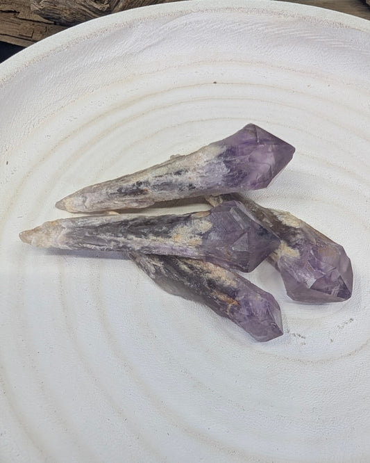 Three natural Amethyst root specimens displayed on a white textured plate with driftwood in the background.