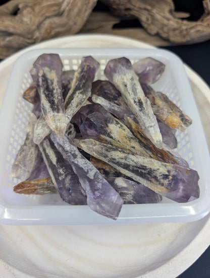 A white basket filled with natural Amethyst root crystals from Bahia, Brazil, showing varied purple terminations.