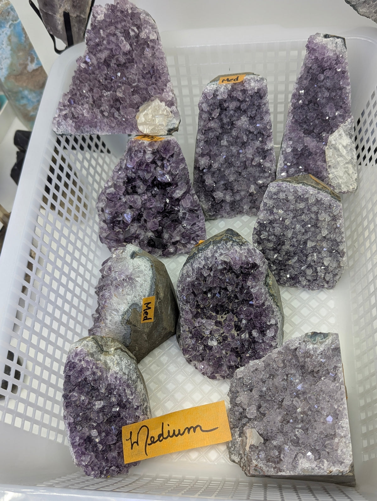 Collection of natural Amethyst cut base vugs in Medium, showcasing deep purple quartz crystals and prominent calcite inclusions on a basalt matrix.