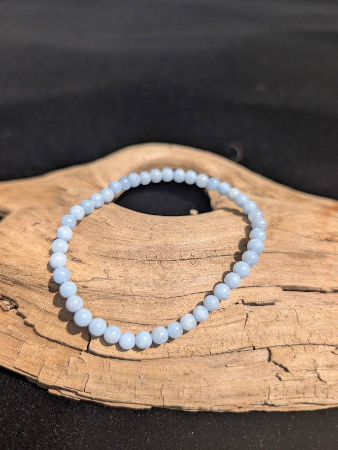 Delicate 4mm Angelite beaded bracelet resting on natural driftwood, displaying an opaque pale blue colouration.