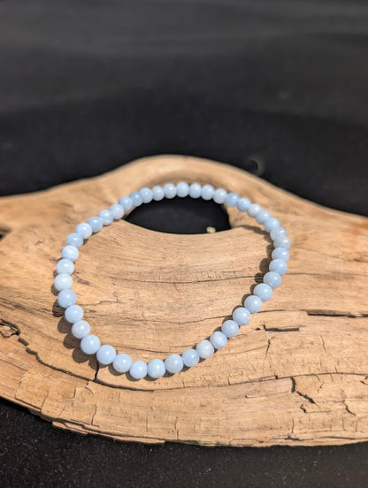 Delicate 4mm Angelite beaded bracelet resting on natural driftwood, displaying an opaque pale blue colouration.