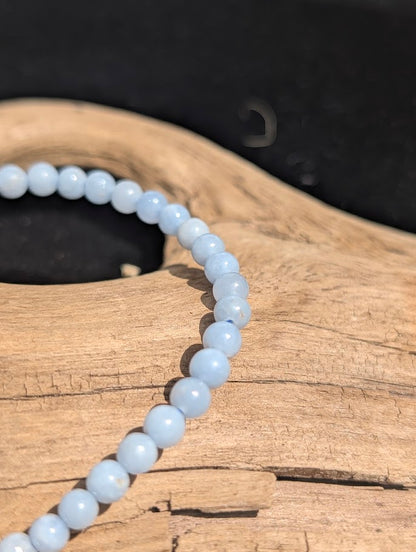 Macro view of polished 4mm pale blue Angelite spherical beads on driftwood.