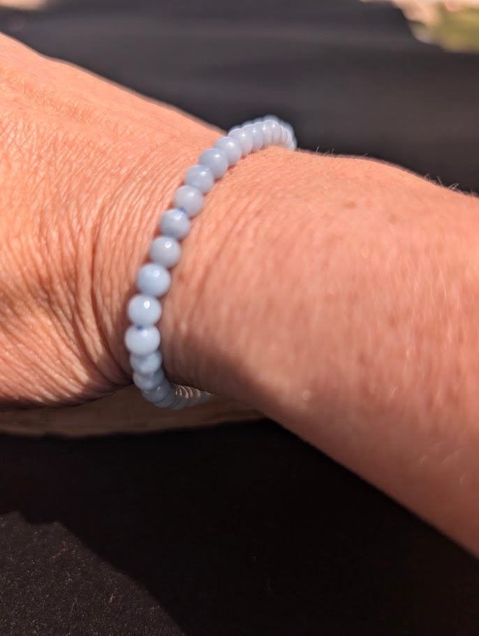 Natural sunlight on a delicate 4mm pale blue Angelite stretch bracelet worn on a wrist.