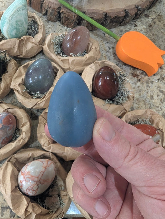 A 2-inch polished Angelite egg held in a hand, displaying a matte, soft pastel blue natural stone surface.