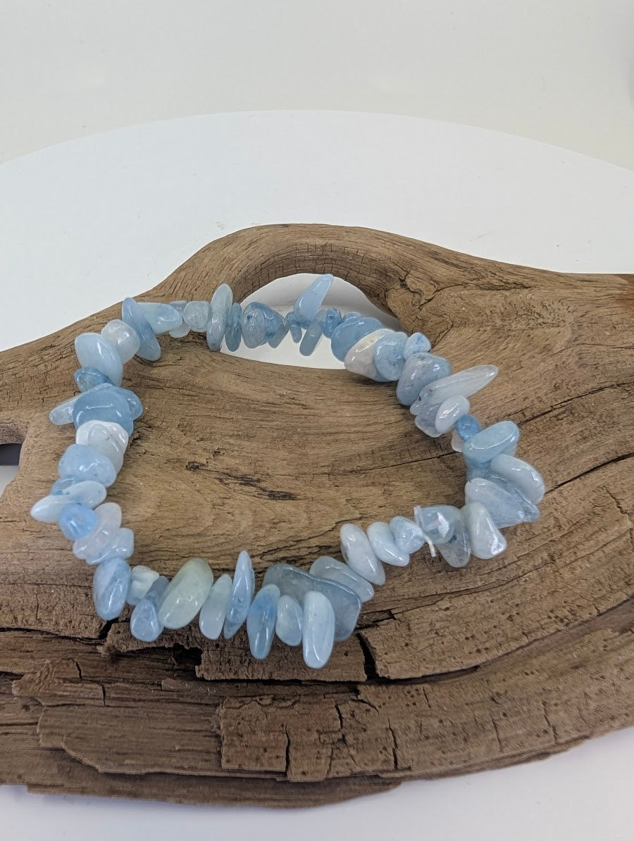 Natural Aquamarine chip bracelet from Brazil displayed on driftwood showing icy blue tumbled stones.