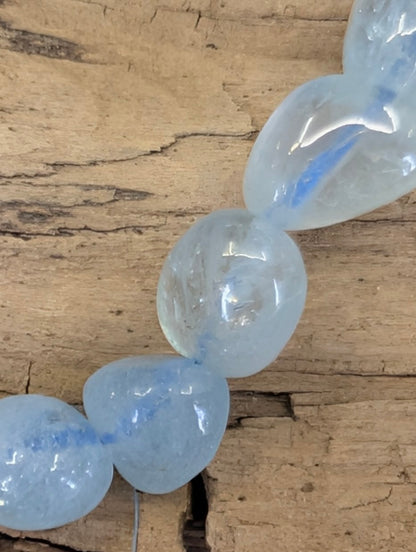 A collection of natural freeform Aquamarine nugget bead bracelets, displayed on a natural wood surface to highlight the organic shape and icy-blue color variation.