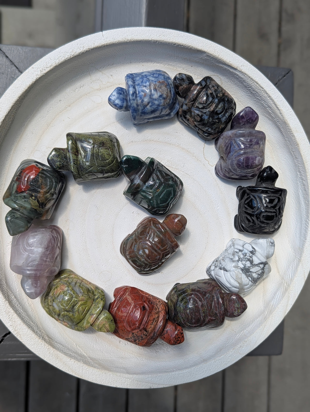 A variety of geometric mineral turtle carvings arranged in a spiral on a white tray, showcasing different stone types like jasper, amethyst, and sodalite.