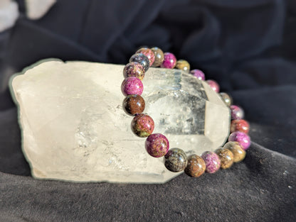 An alternate display angle of the premium 9.5mm Atlantisite beaded stretch bracelet resting on a presentation surface, emphasizing the continuous polish and natural matrix colours under balanced lighting.